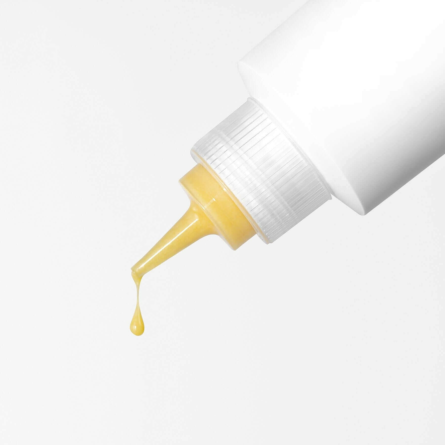 Close-up of yellow liquid dripping from white bottle against white background.